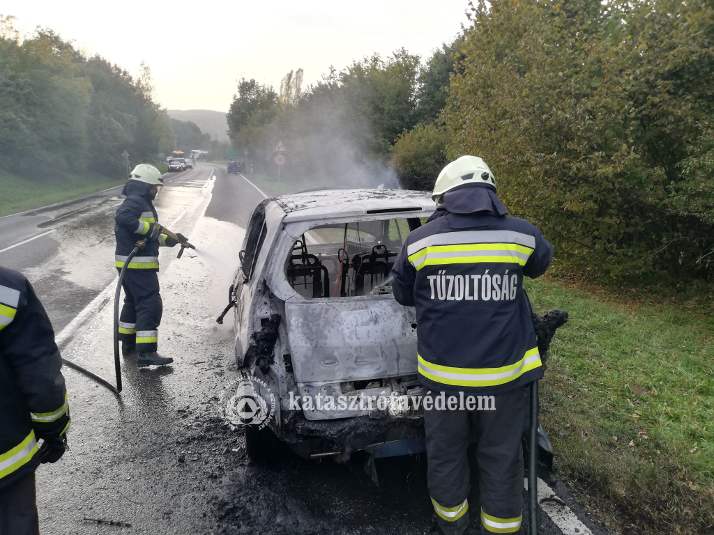 tűzoltók vízzel hűtik a kiégett személyautót