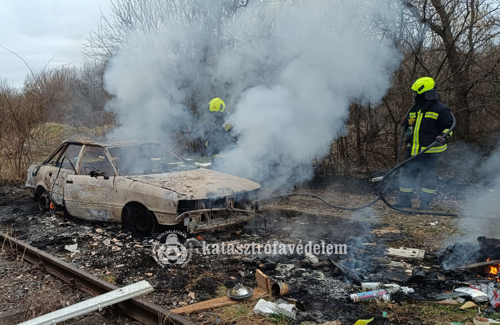 tűzoltók oltják a teljesen kiégett személyautót és környezetét