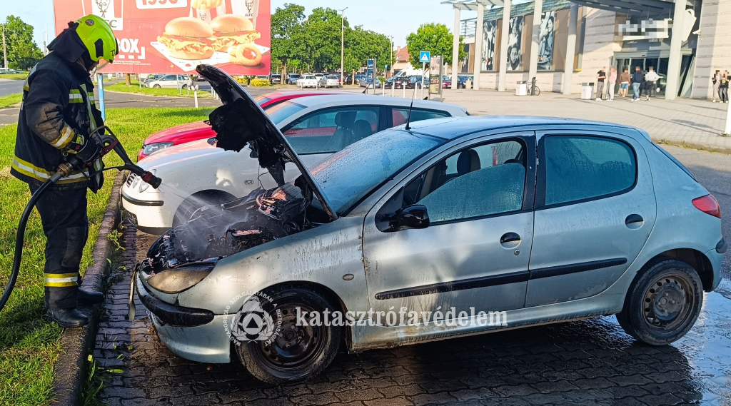 tűzoltó oltja a személyautó motorterét