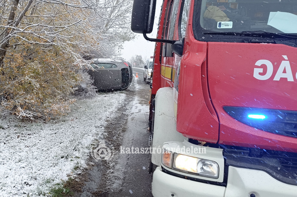 előtérben tűzoltóautó, háttérben felborult autó az árokban