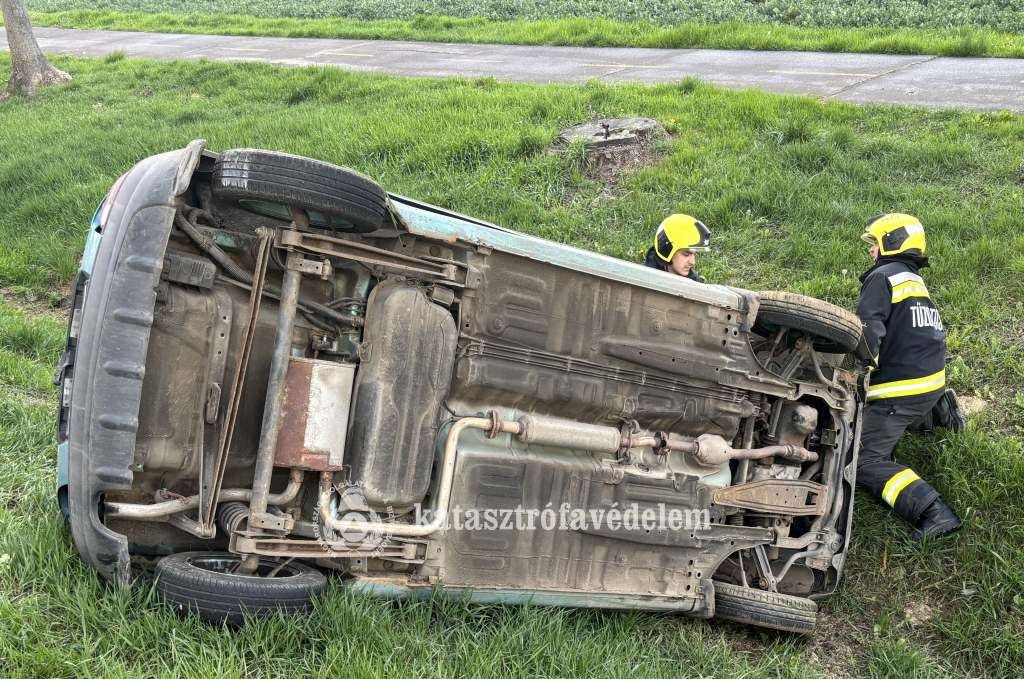 autó az oldalán, mellette tűzoltók