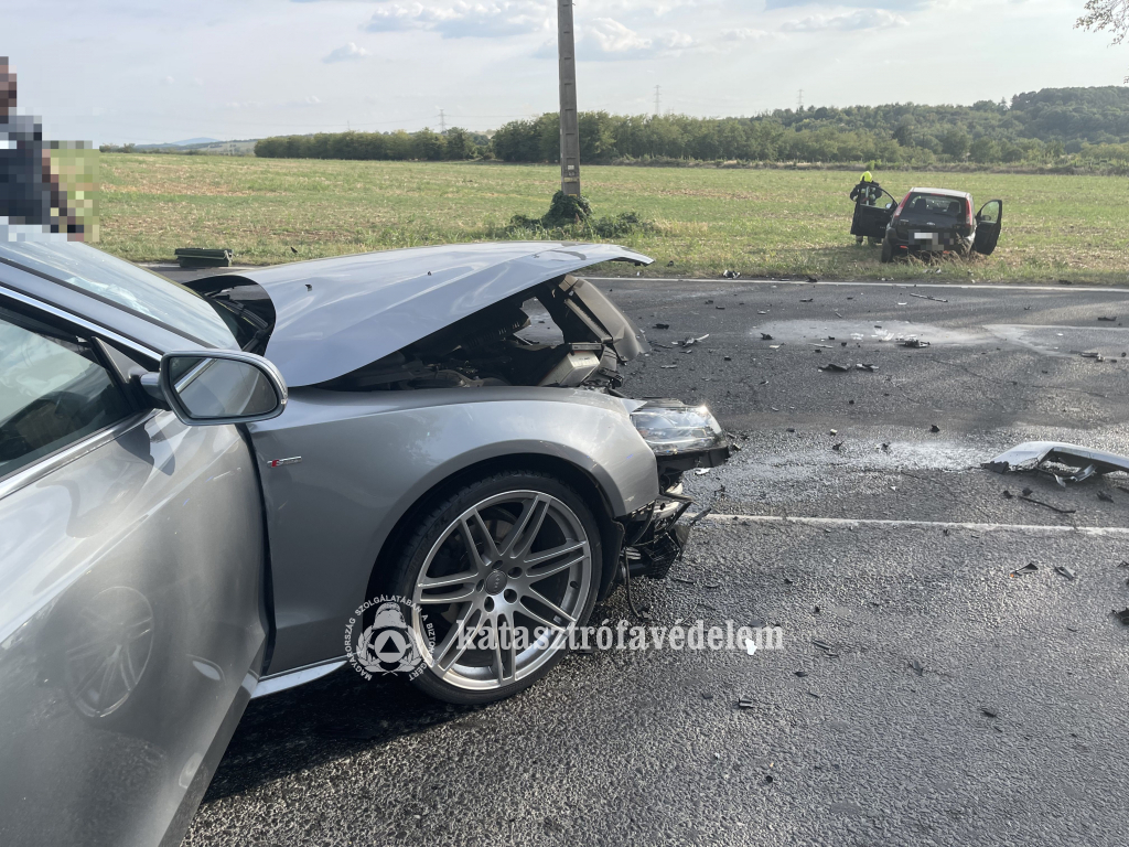 előtérben a törött orrú autó, hátul a füves részen a másik