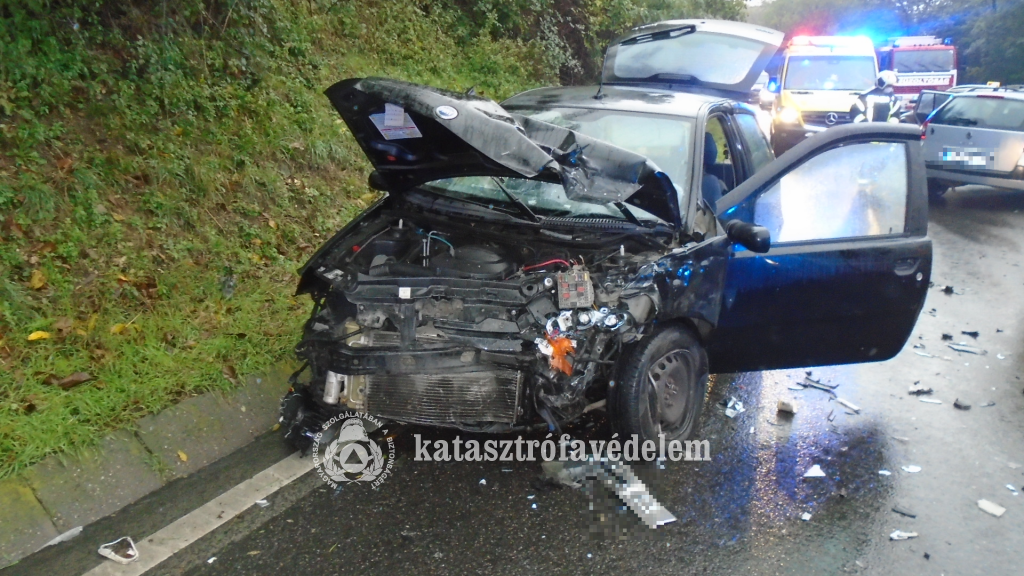 összetört autó, mögötte mentő és tűzoltó autó