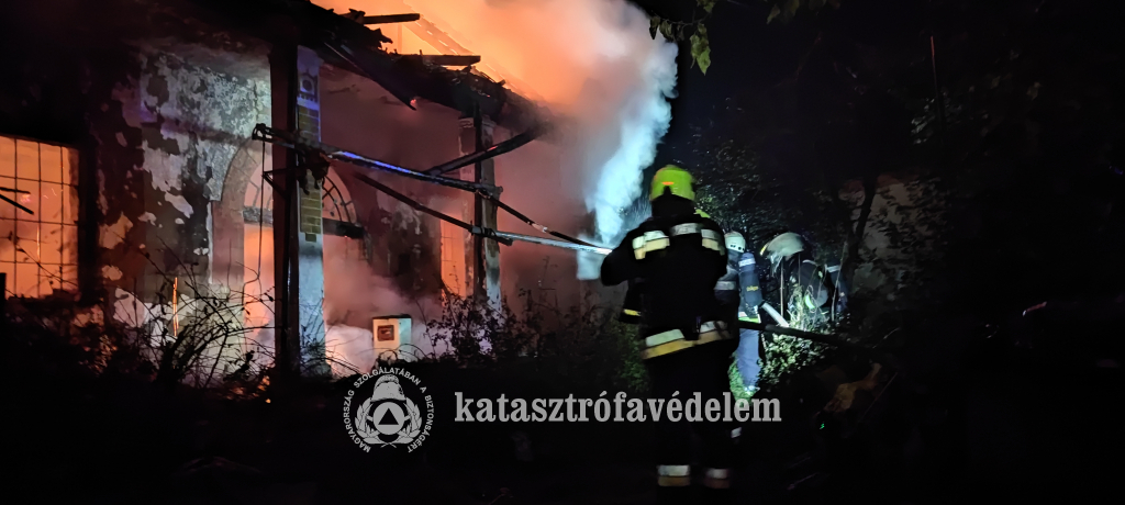 három tűzoltó oltja a lángoló épületet